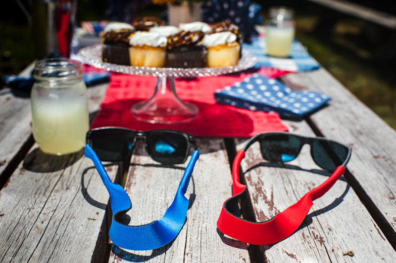 Two Croakies eyewear retainers propped on a picnic table